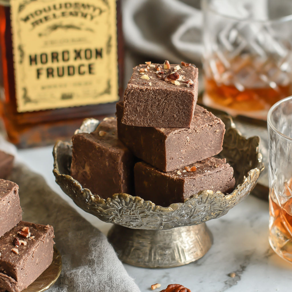 A bottle of whiskey and a bowl of chocolate squares.