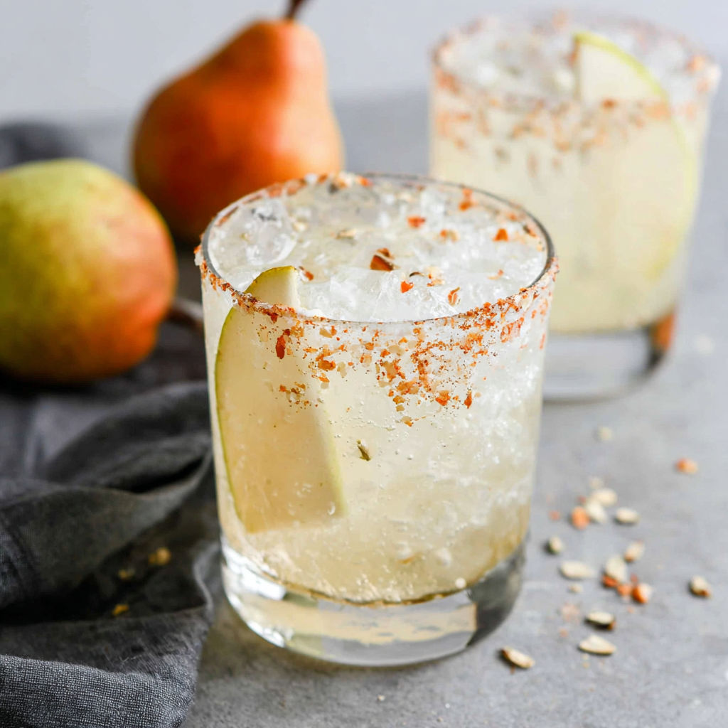 A glass of a cocktail with a slice of lemon and a pear.