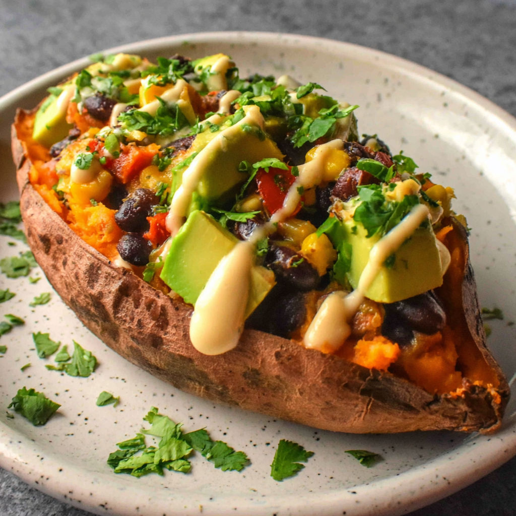 A baked potato with toppings and sauce.