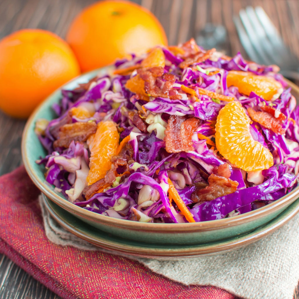 A bowl of salad with bacon and oranges.