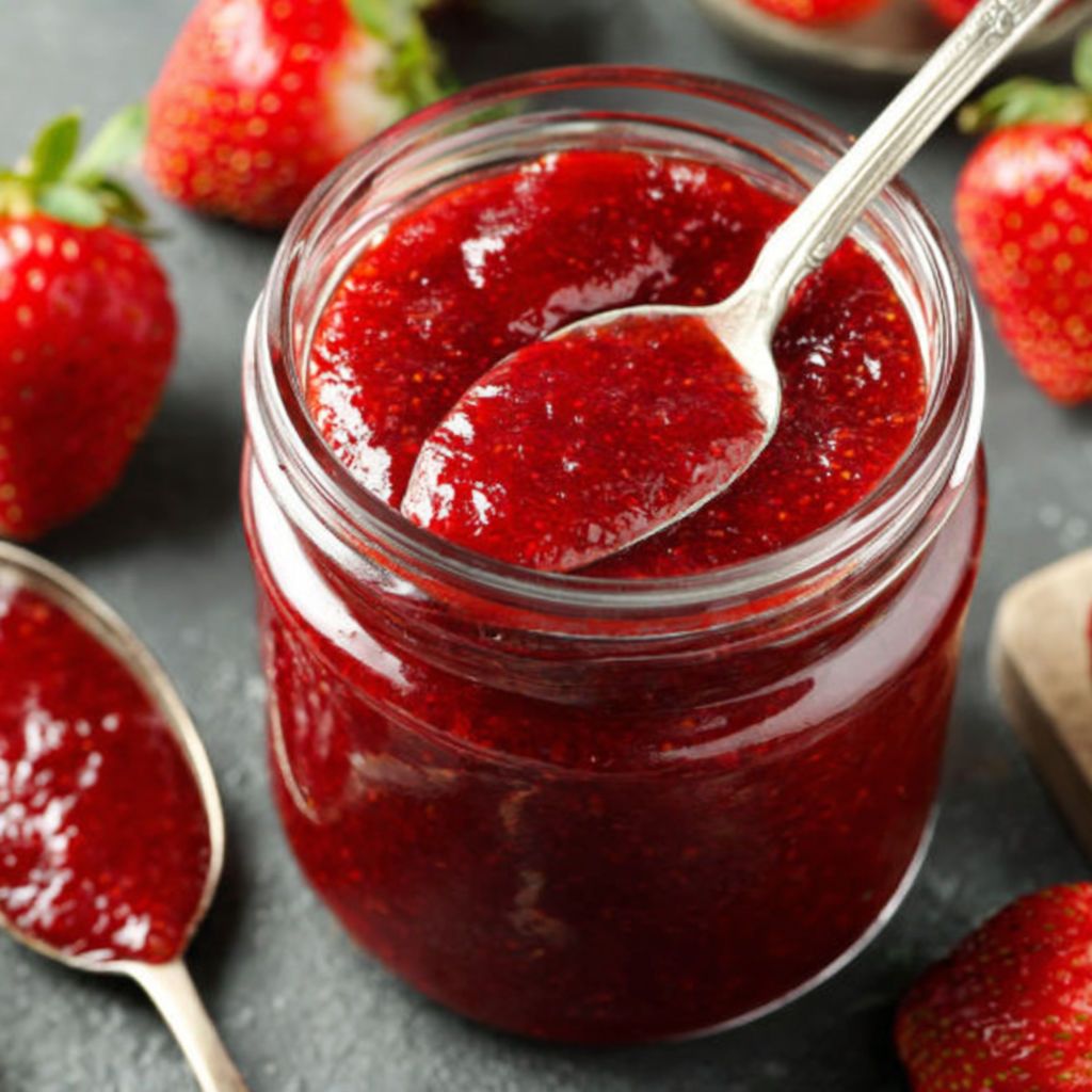 A jar of strawberry jam with a spoon in it.