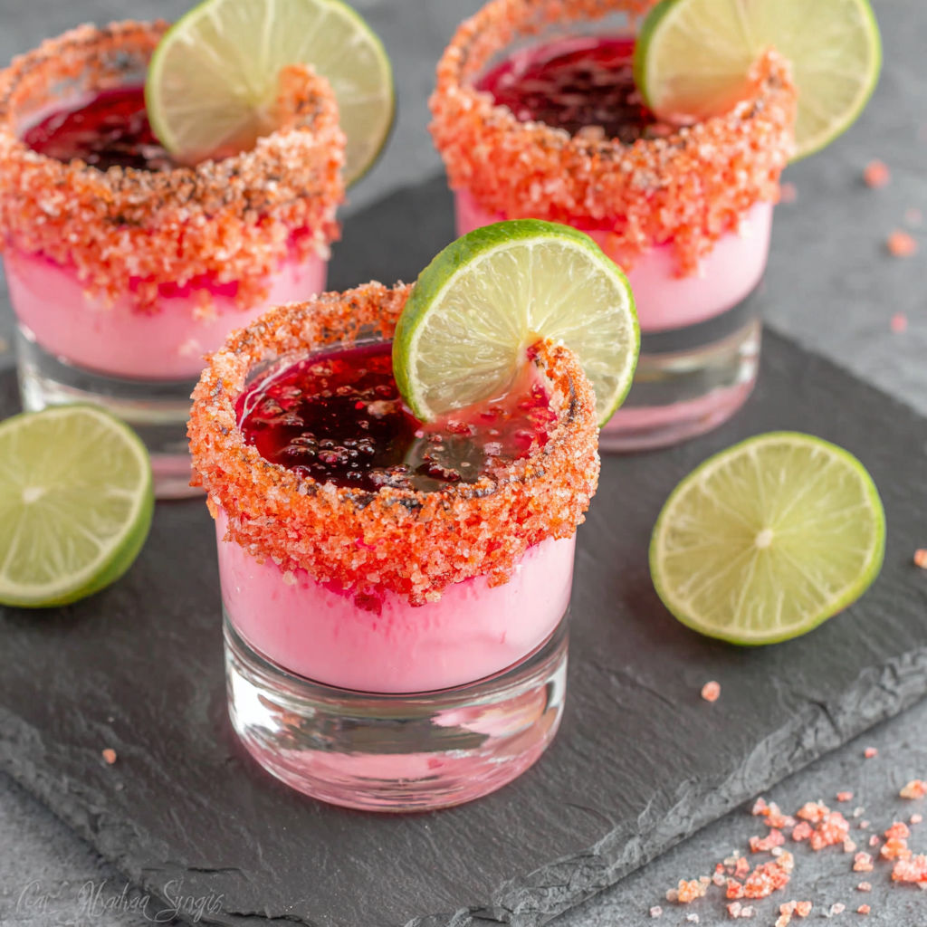 Two glasses of pink drink with lime wedges.