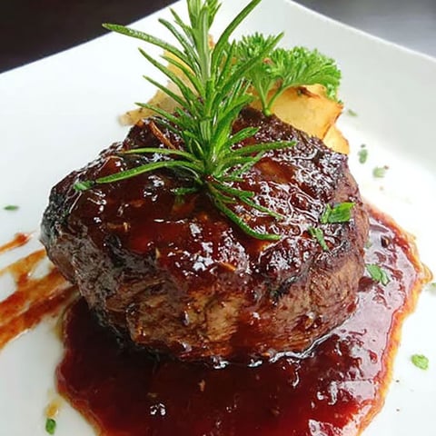 A piece of meat with a green garnish on a plate.