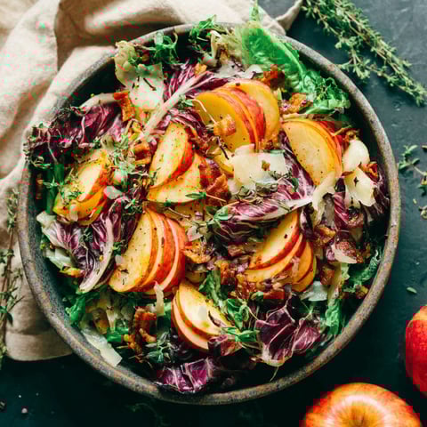 A bowl of salad with apples, lettuce, and bacon.