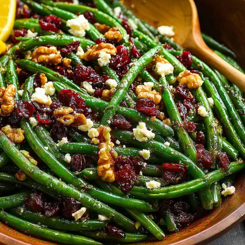 A bowl of green beans with feta cheese and red berries.