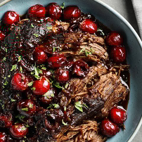 A bowl of beef stew with cherries and green herbs.