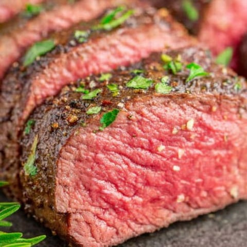 A close up of a piece of meat with herbs on top.