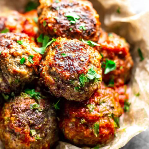 A bowl of meatballs with green herbs on top.