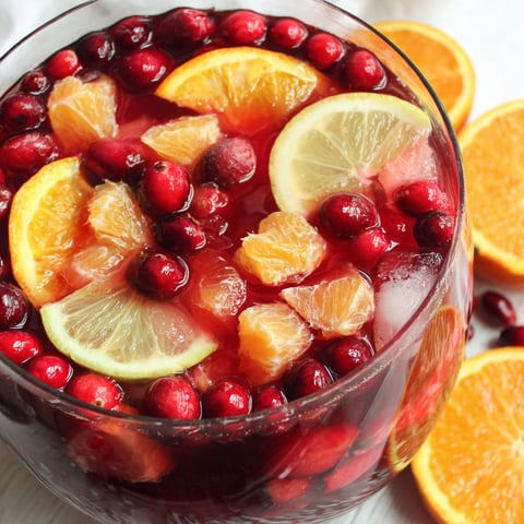 A glass of red wine with oranges and cranberries.