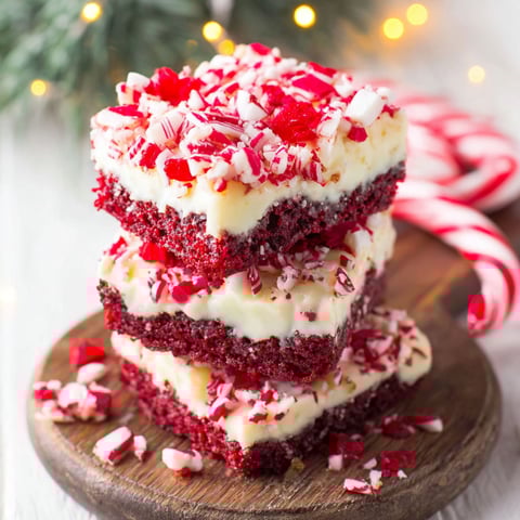 A stack of red velvet cake with white frosting and red sprinkles.