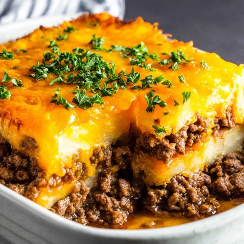 A dish of meat and potatoes with a white plate underneath.