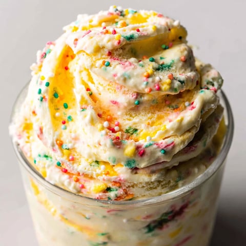 A glass of yellow and white frosting with sprinkles.