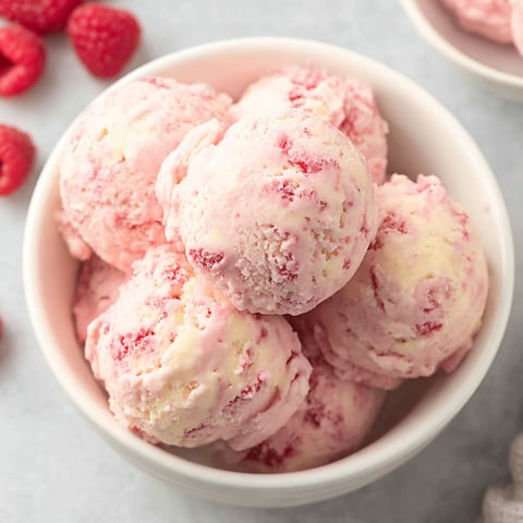 A bowl of pink ice cream with raspberries on top.