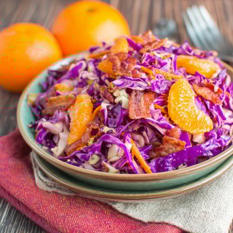 A bowl of salad with bacon and oranges.