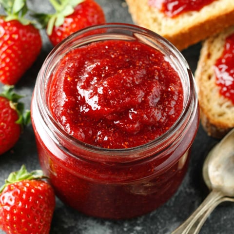 A jar of strawberry jam with a spoon in it.