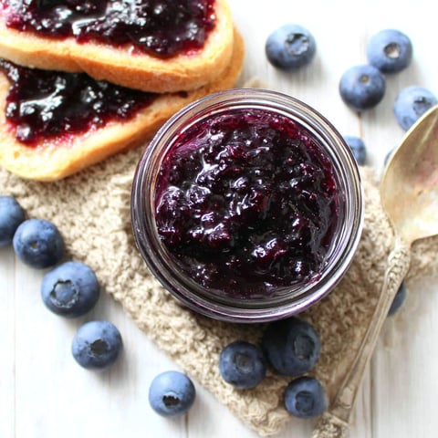 A jar of blueberry jam on a table.