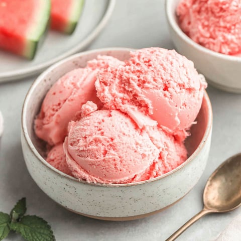 A bowl of pink ice cream with a spoon in it.