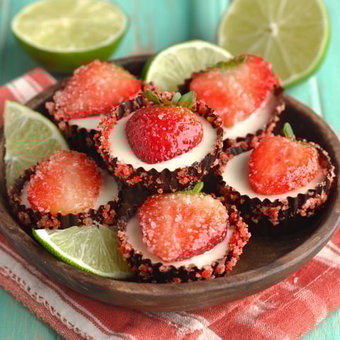 A plate of strawberry desserts with limes on the side.