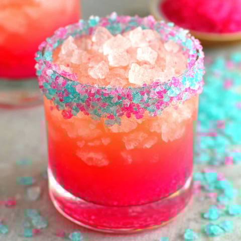 A glass of pink drink with a sprinkle of sugar on top.